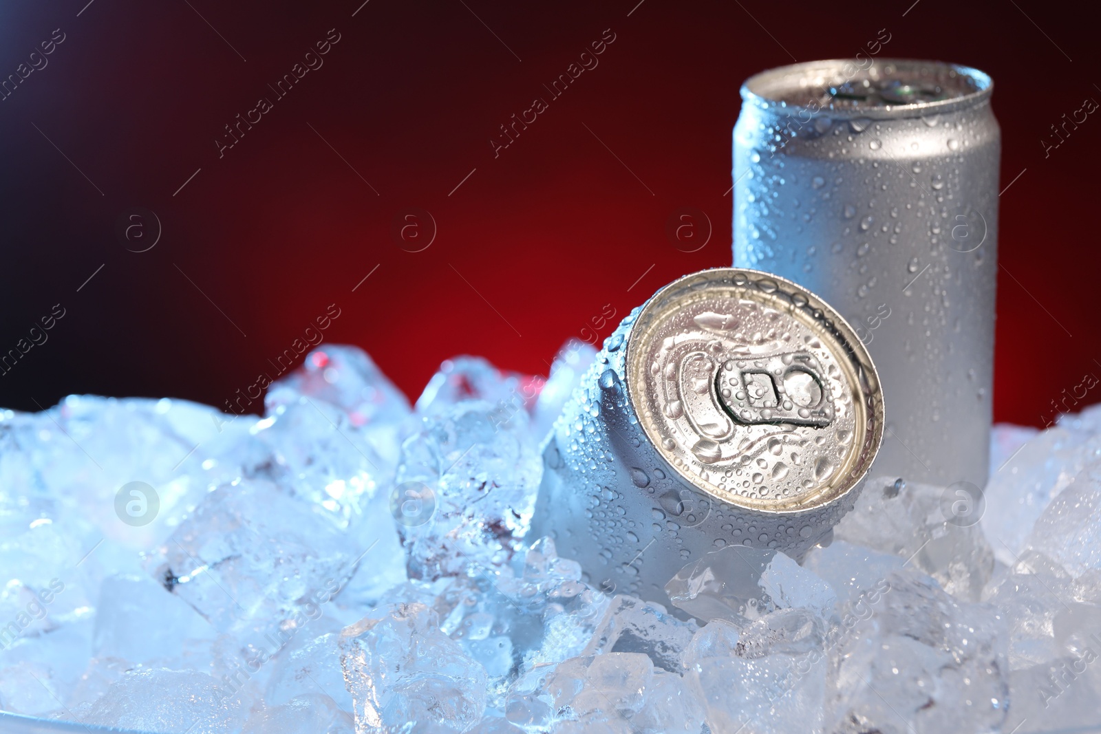 Refreshing drinks in cans on ice cubes against dark red background, closeup Photo of Refreshing drinks in cans on ice cubes against dark red background, closeup