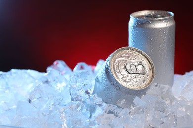 Photo of Refreshing drinks in cans on ice cubes against dark red background, closeup