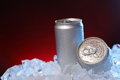 Photo of Refreshing drinks in cans on ice cubes against dark red background, closeup. Space for text