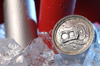 Photo of Refreshing drinks in cans on ice cubes against dark red background, closeup