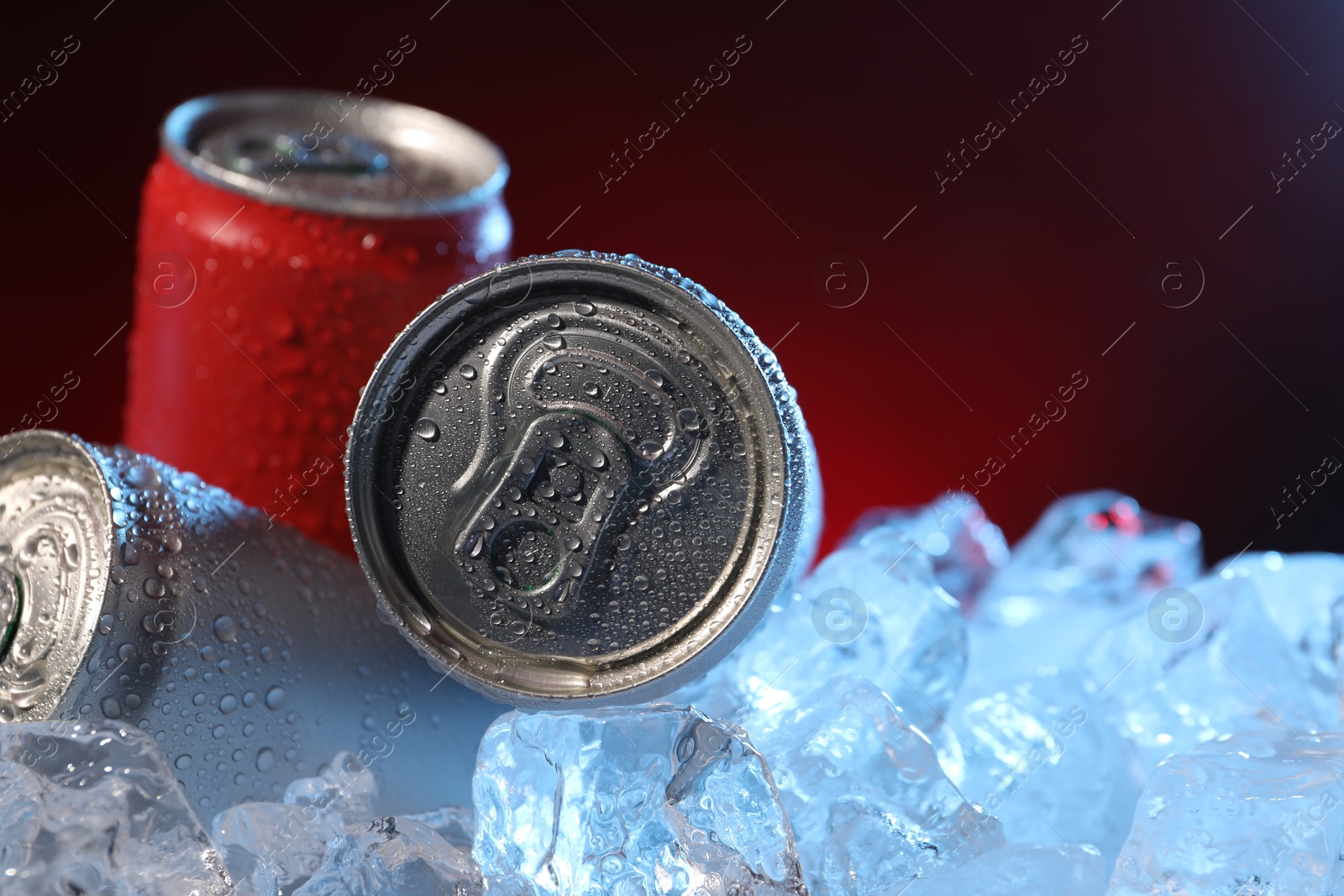 Refreshing drinks in cans on ice cubes against dark red background, closeup. Space for text Photo of Refreshing drinks in cans on ice cubes against dark red background, closeup. Space for text