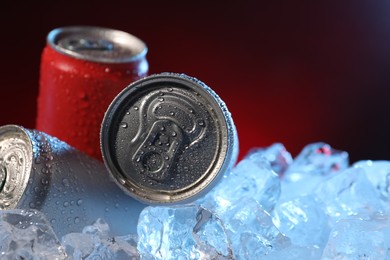 Photo of Refreshing drinks in cans on ice cubes against dark red background, closeup. Space for text
