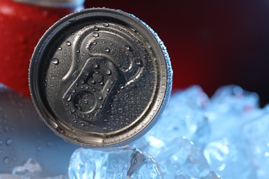 Photo of Refreshing drinks in cans on ice cubes against dark red background, closeup. Space for text