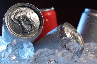 Photo of Refreshing drinks in cans on ice cubes against dark background, closeup
