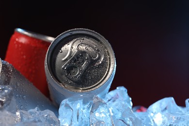 Photo of Refreshing drinks in cans on ice cubes against dark background, closeup. Space for text