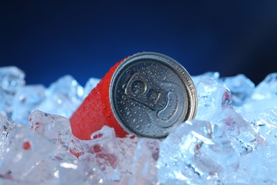 Photo of Refreshing drink in can on ice cubes against dark blue background, closeup