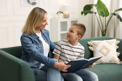 Photo of Mother and son reading book on sofa at home