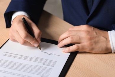 Photo of Man putting signature on document at wooden table, closeup