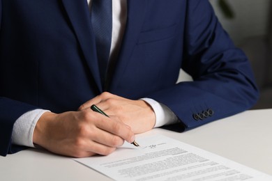 Photo of Man putting signature on document at white table, closeup