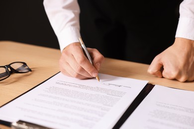 Photo of Man putting signature on document at wooden table, closeup