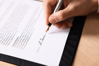 Photo of Man putting signature on document at wooden table, closeup