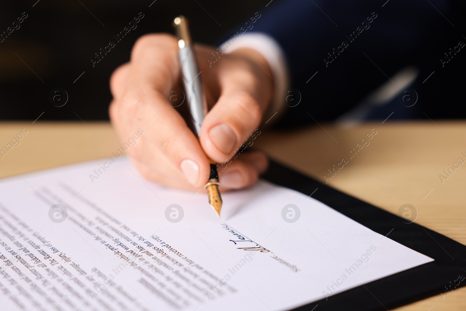 Photo of Man putting signature on document at table, closeup