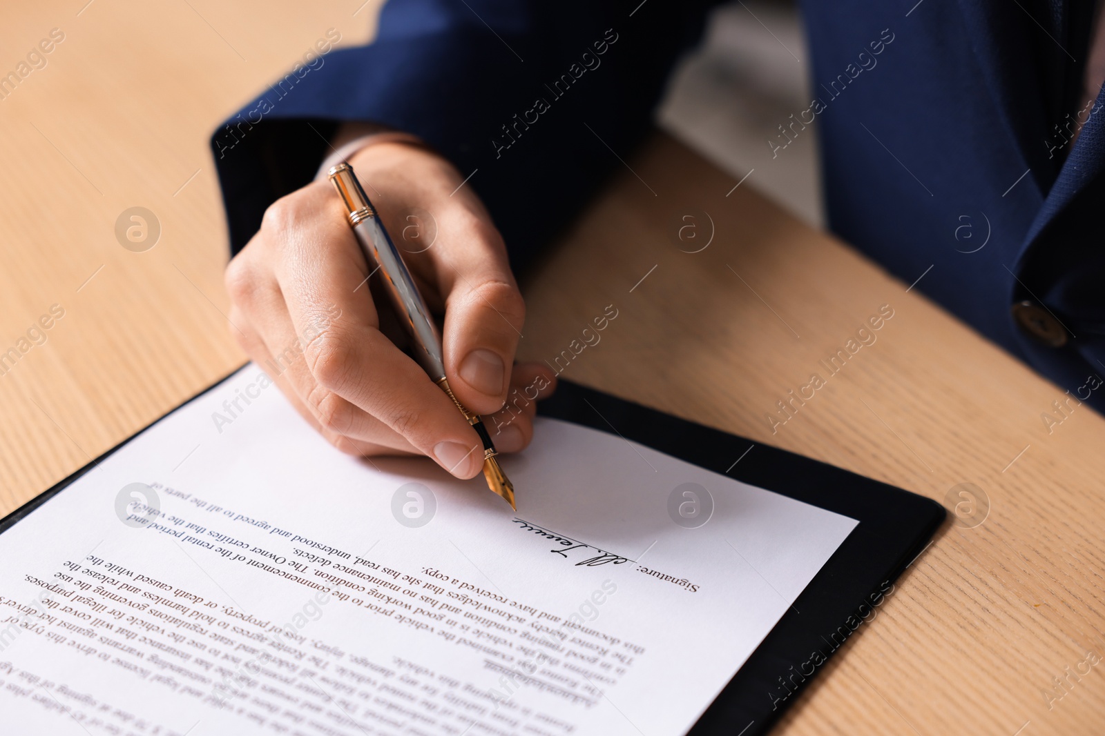 Photo of Man putting signature on document at wooden table, closeup