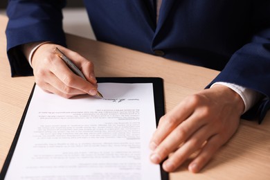 Photo of Man putting signature on document at wooden table, closeup