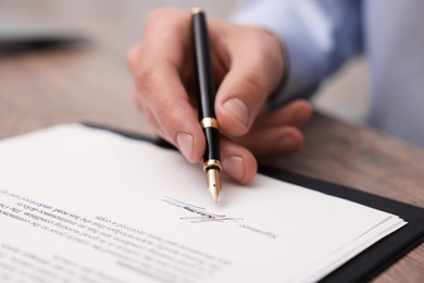 Photo of Man putting signature on document at table, closeup