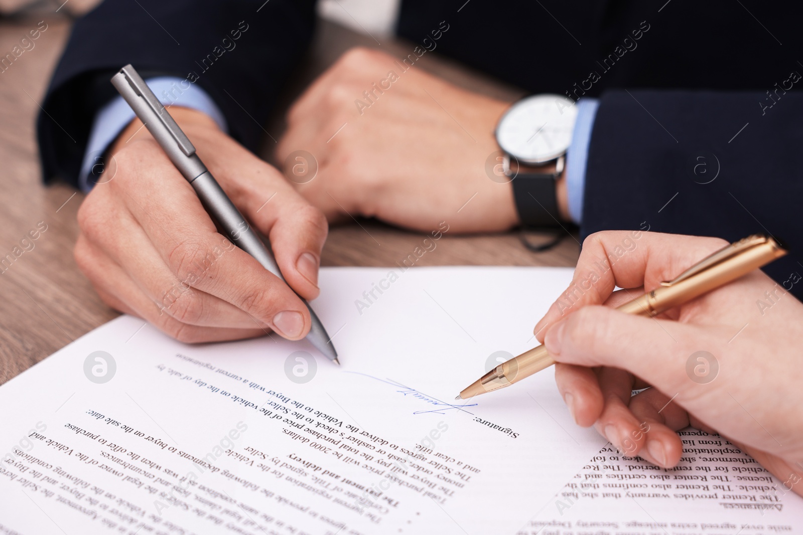 Photo of Woman pointing at document and man putting signature at table, closeup