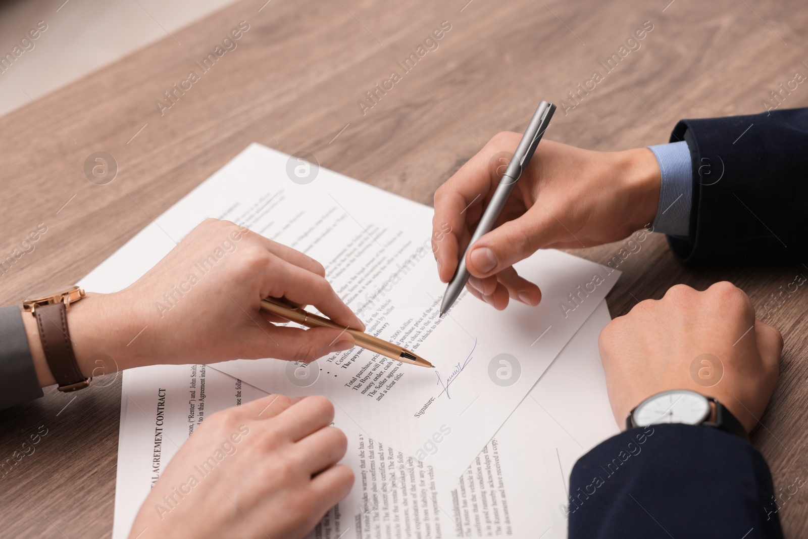 Photo of Woman pointing at document and man putting signature at wooden table, closeup