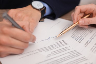 Photo of Woman pointing at document and man putting signature at table, closeup