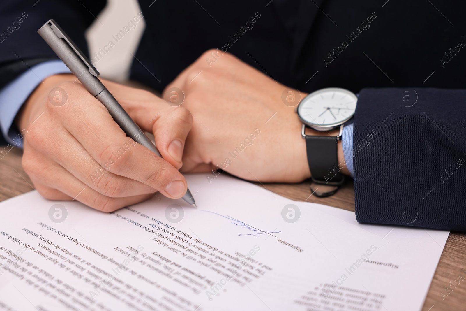 Photo of Man putting signature on document at table, closeup