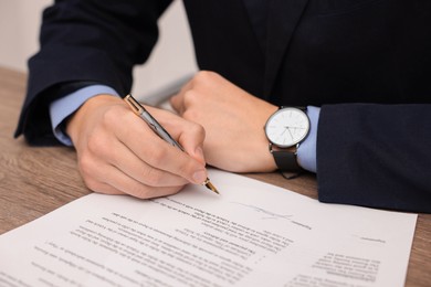 Photo of Man putting signature on document at wooden table, closeup