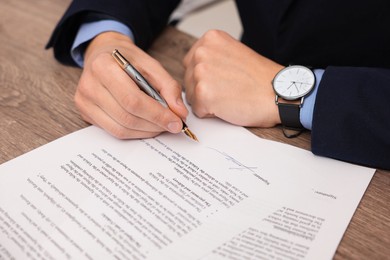 Photo of Man putting signature on document at wooden table, closeup