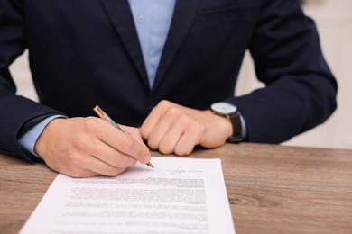 Photo of Man putting signature on document at wooden table, closeup