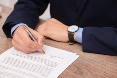 Photo of Man putting signature on document at wooden table, closeup