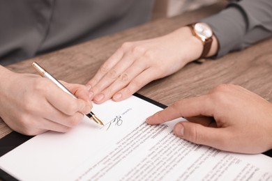 Photo of Man pointing at document and woman putting signature at wooden table, closeup