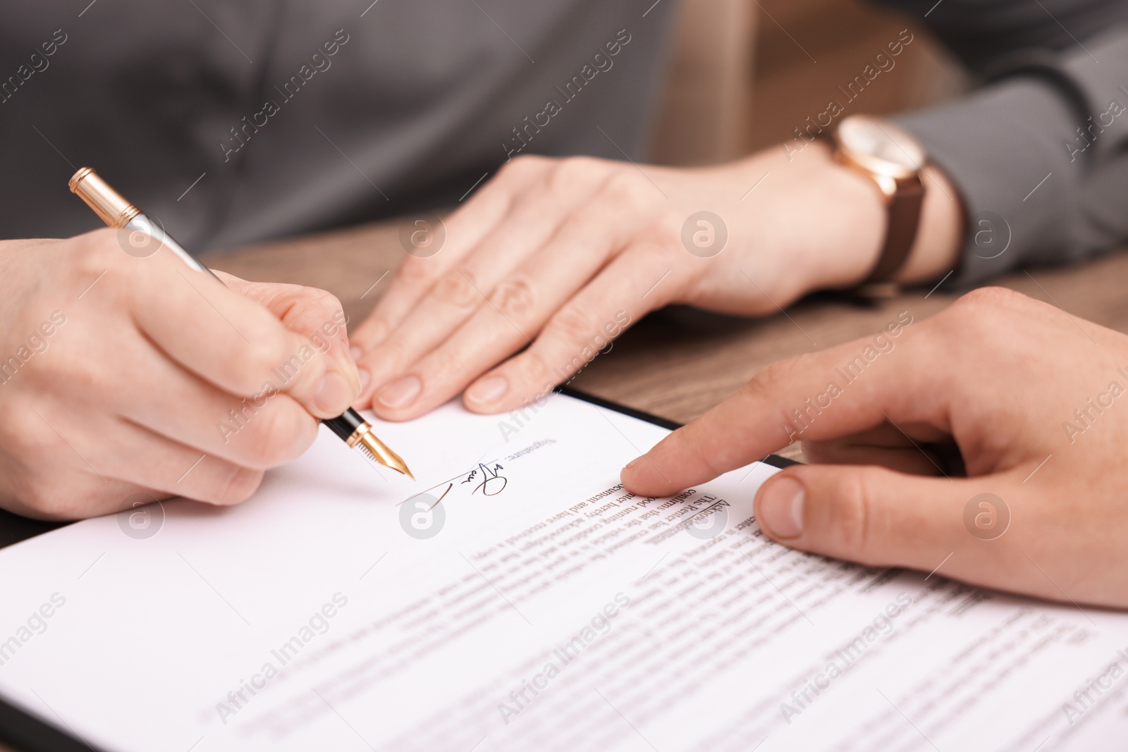 Photo of Man pointing at document and woman putting signature at table, closeup