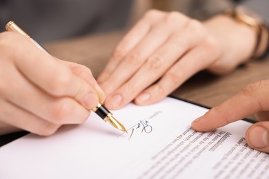 Photo of Man pointing at document and woman putting signature at table, closeup