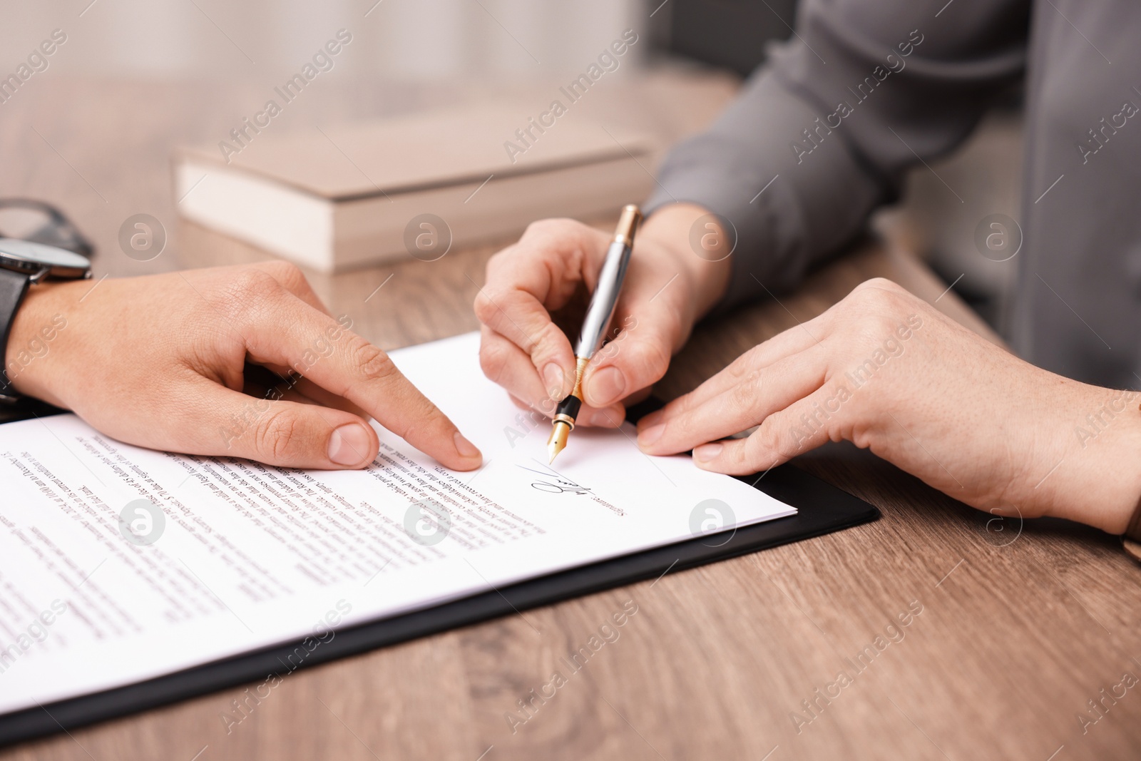 Photo of Man pointing at document and woman putting signature at wooden table, closeup