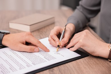 Photo of Man pointing at document and woman putting signature at wooden table, closeup