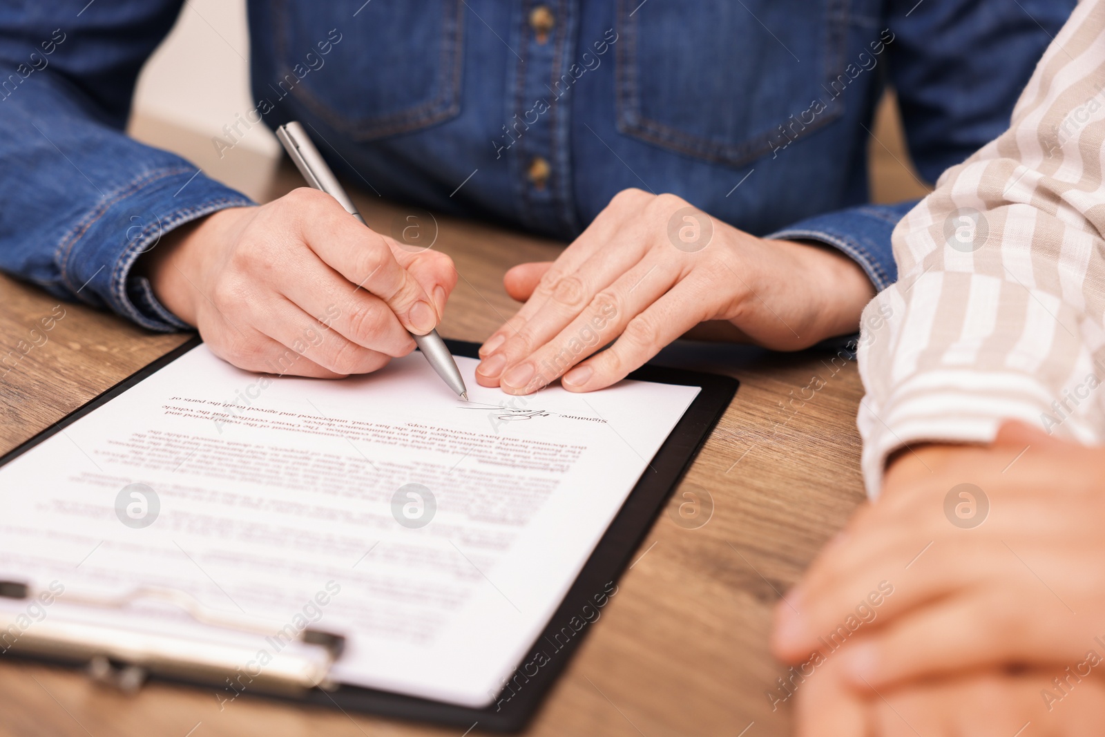 Photo of Woman putting signature on document at wooden table, closeup