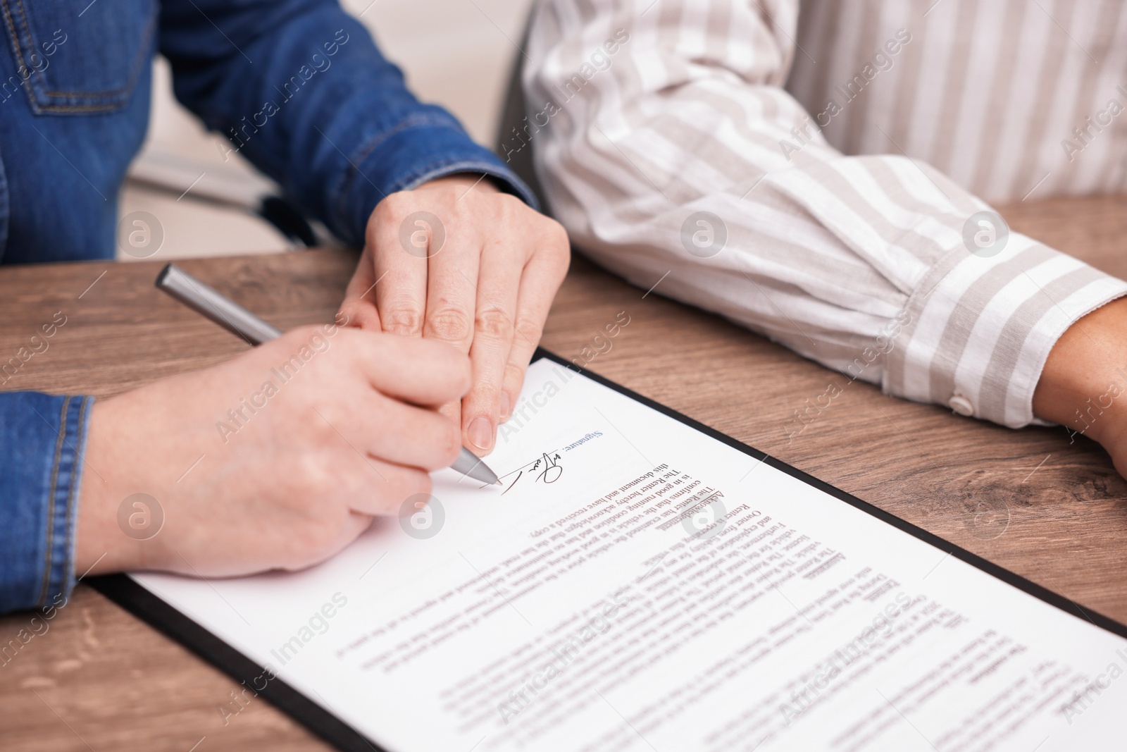 Photo of Woman putting signature on document at wooden table, closeup