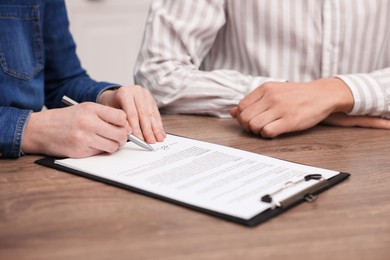 Photo of Woman putting signature on document at wooden table, closeup