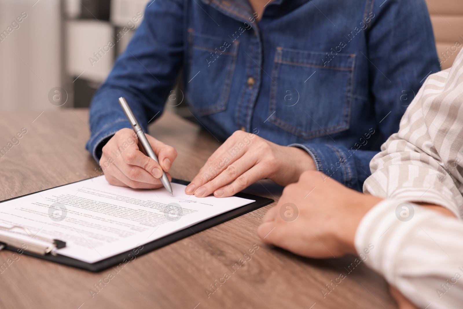 Photo of Woman putting signature on document at wooden table, closeup