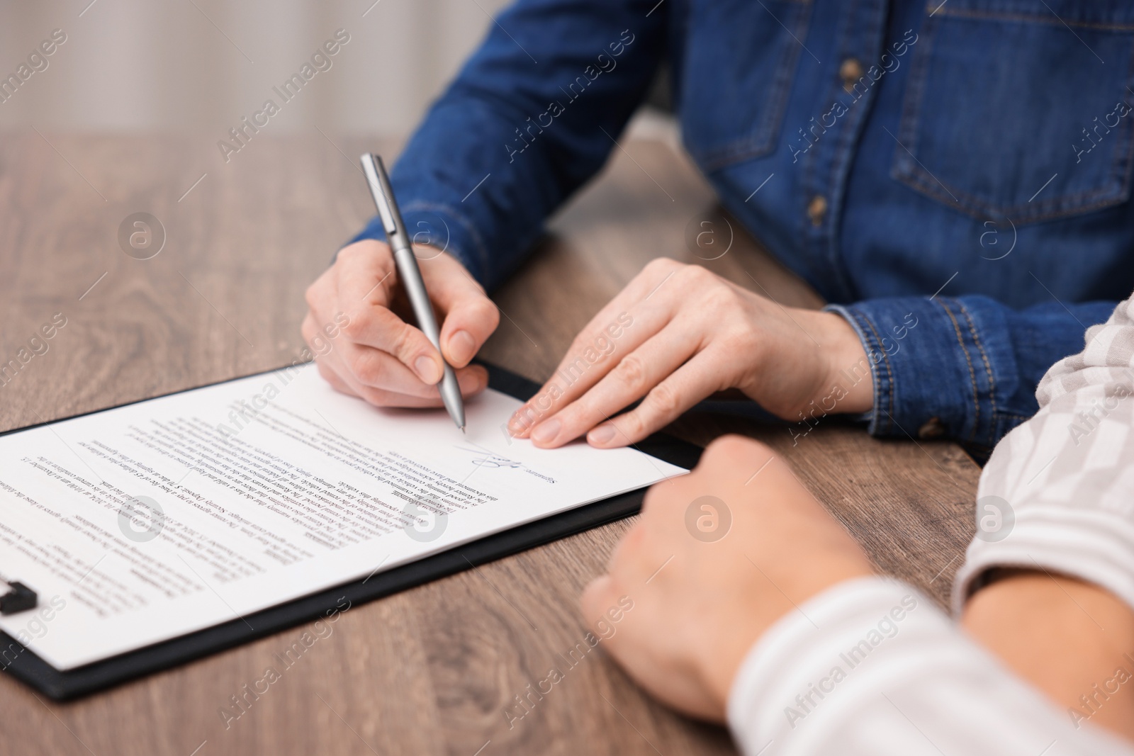 Photo of Woman putting signature on document at wooden table, closeup