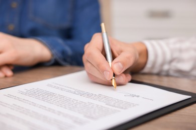 Photo of Man putting signature on document at table, closeup