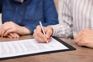 Photo of Man putting signature on document at wooden table, closeup