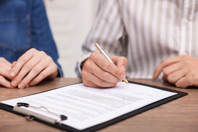 Photo of Man putting signature on document at wooden table, closeup