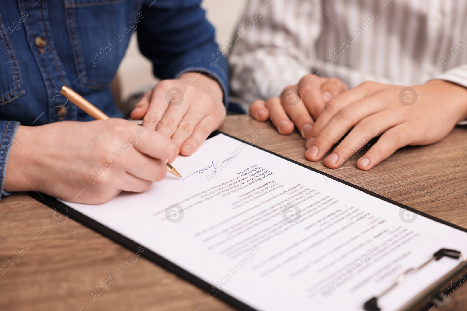 Photo of Woman putting signature on document at wooden table, closeup