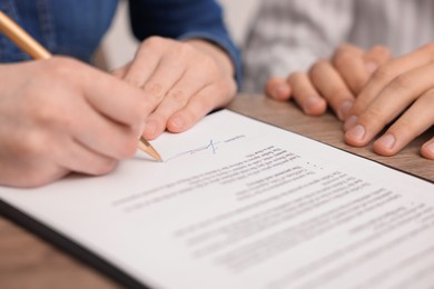 Photo of Woman putting signature on document at table, closeup