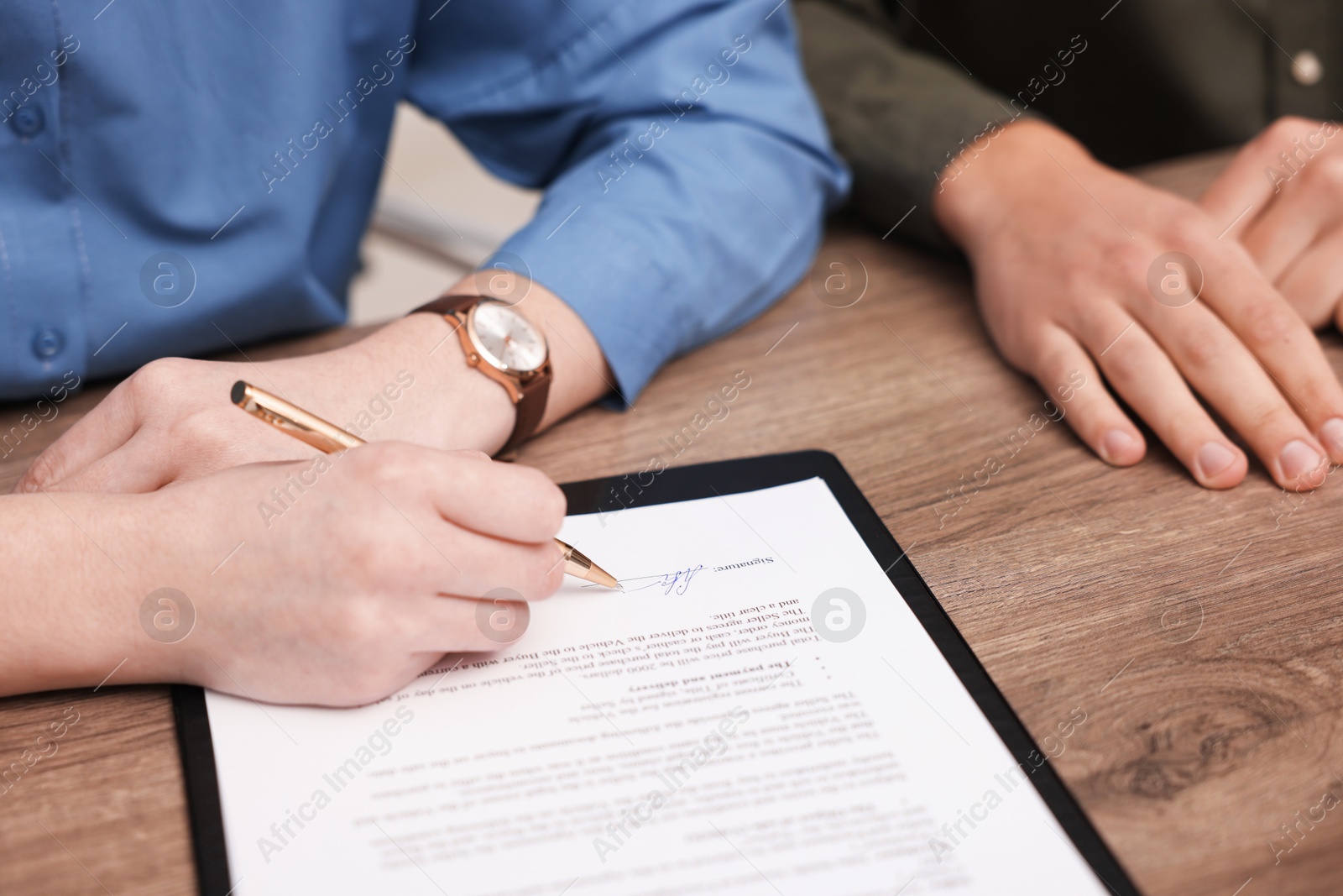 Photo of Woman putting signature on document at wooden table, closeup