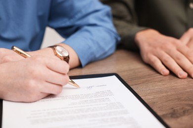 Photo of Woman putting signature on document at wooden table, closeup