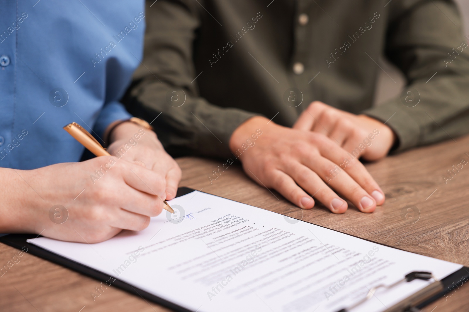 Photo of Woman putting signature on document at wooden table, closeup