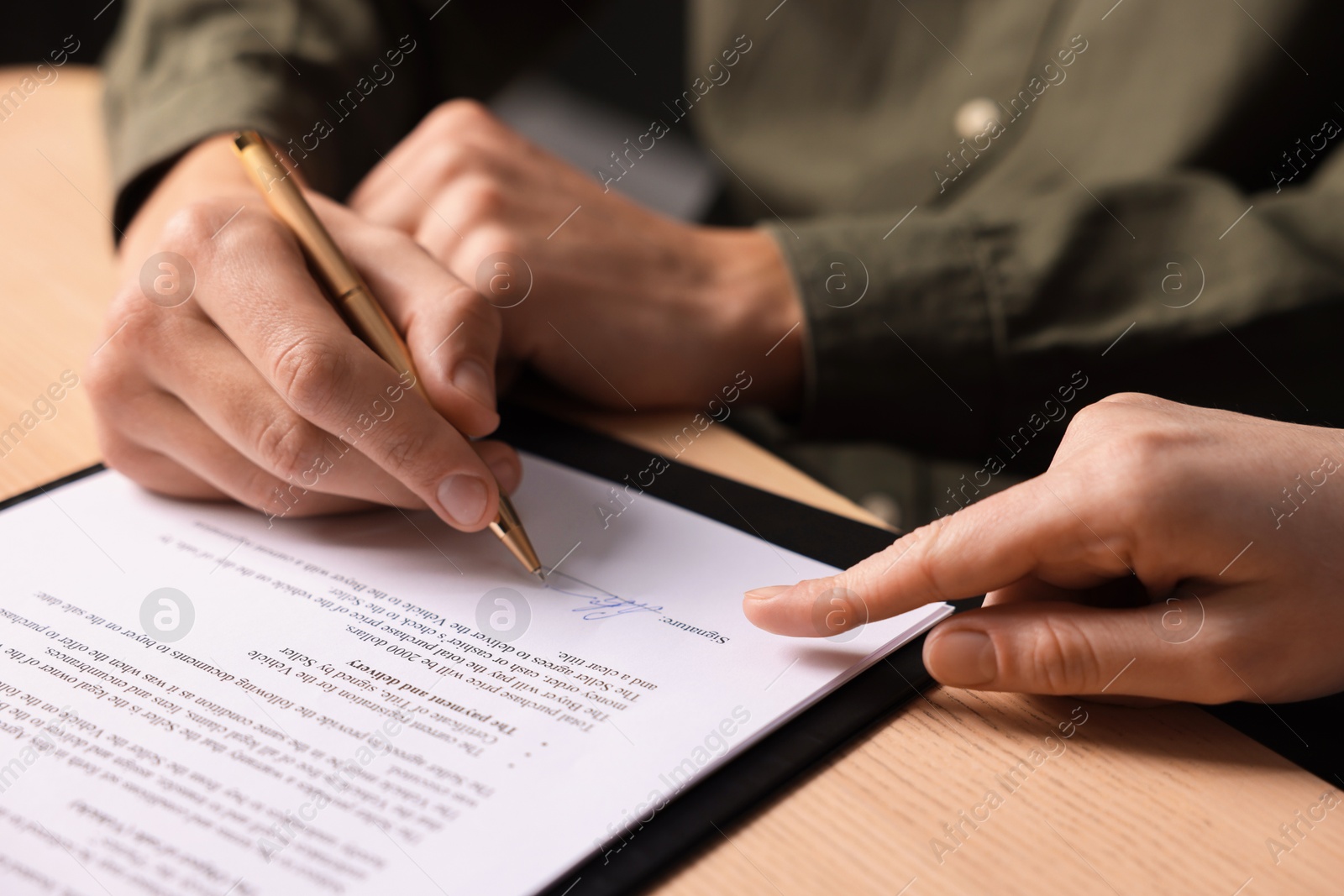 Photo of Woman pointing at document and man putting signature at wooden table, closeup