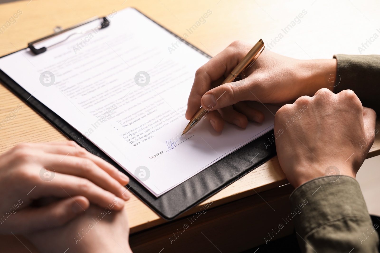 Photo of Man putting signature on document at wooden table, closeup