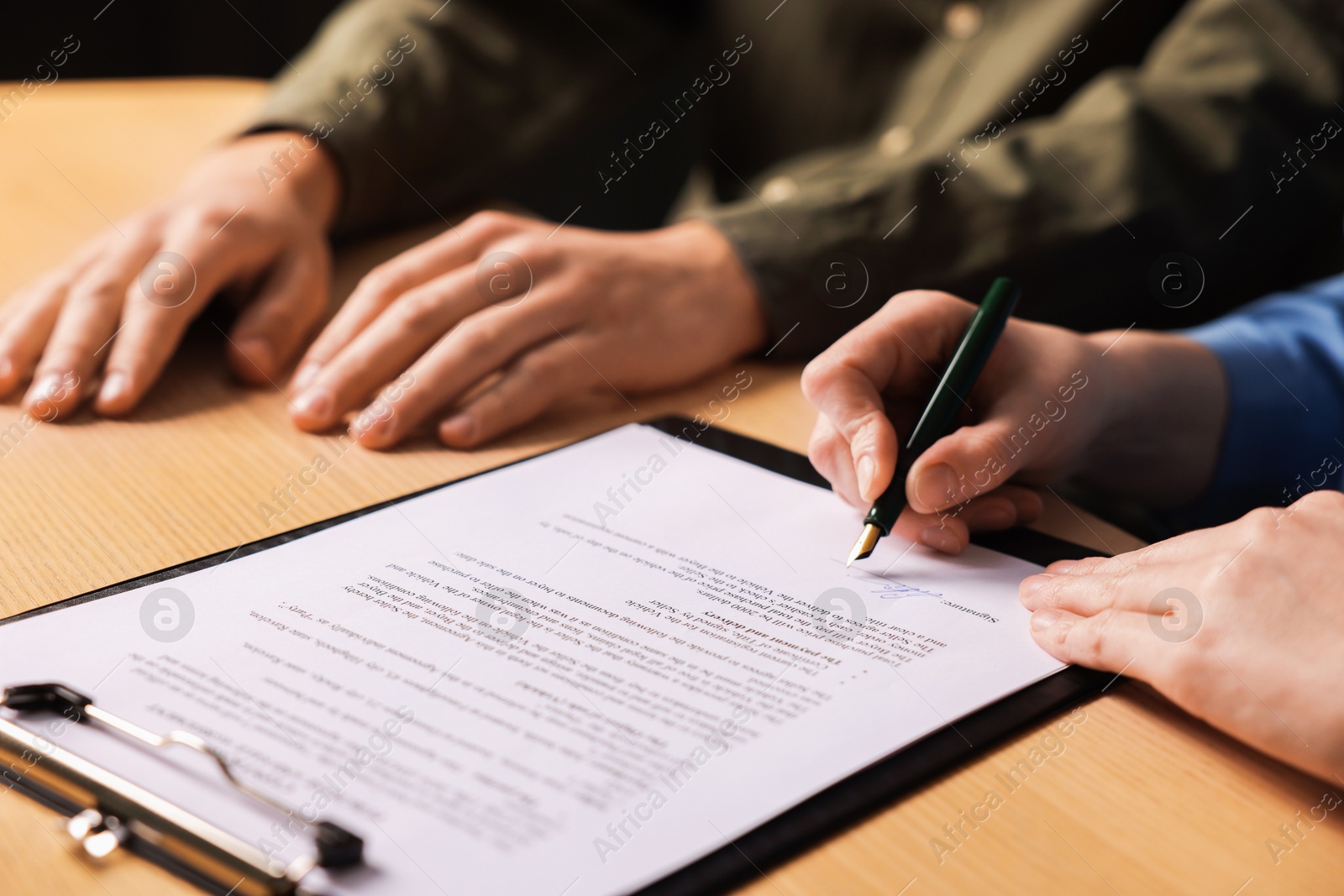 Photo of Woman putting signature on document at wooden table, closeup