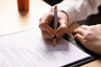 Photo of Woman putting signature on document at table, closeup