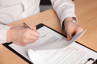 Photo of Woman putting signature on document at wooden table, closeup